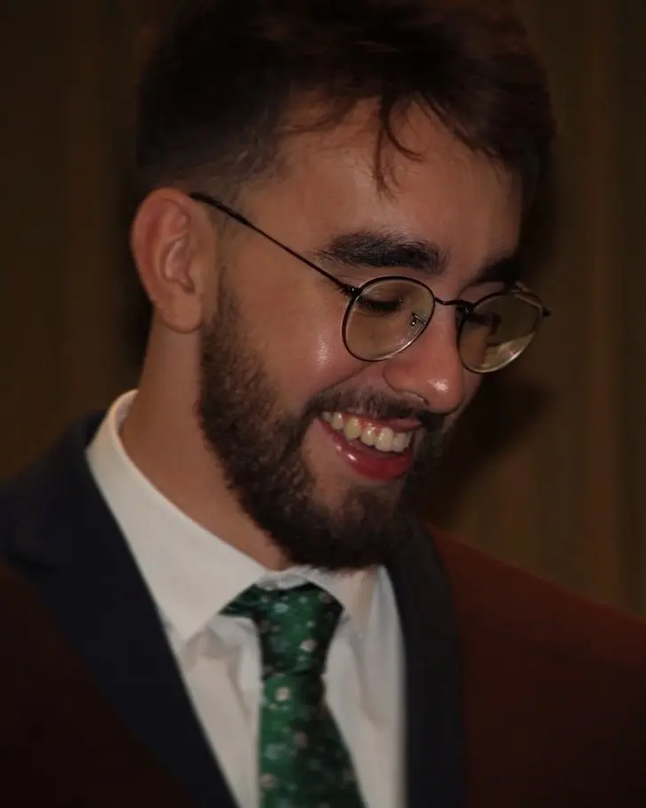 Pedro on his graduation day, wearing a suit and a green tie, smiling.