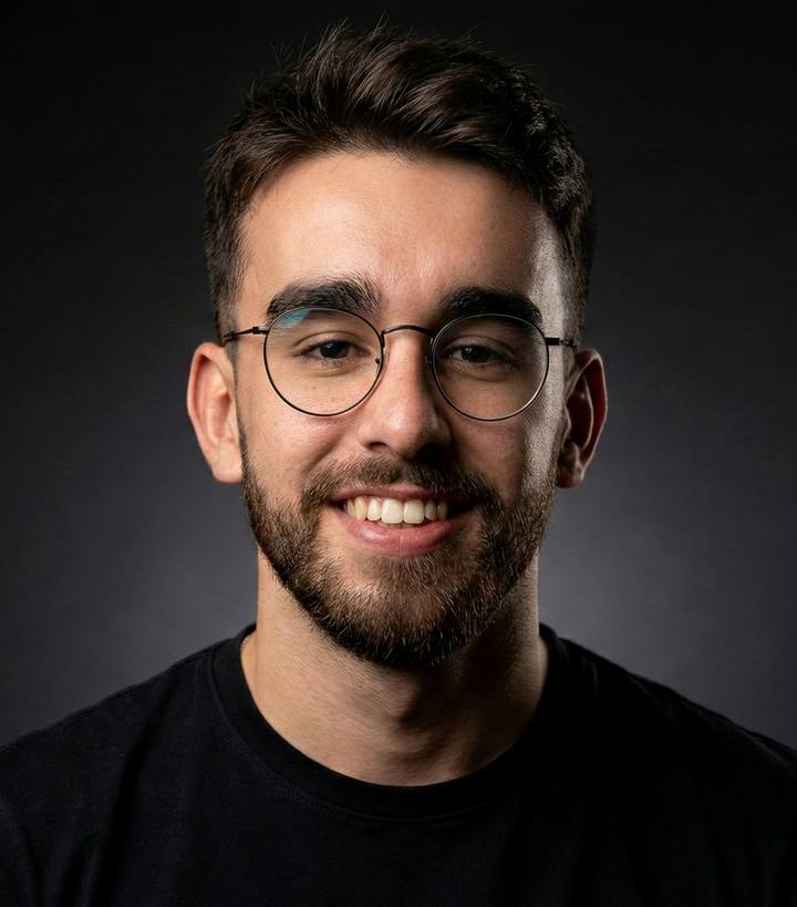 Pedro Luis Soto Santos smiling, wearing round glasses and a black T-shirt, on a dark background.